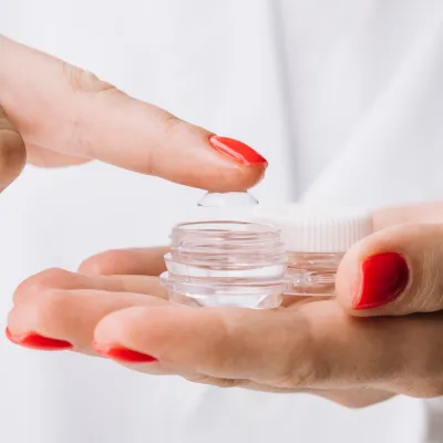 A contact lens balanced on a fingertip beside its case